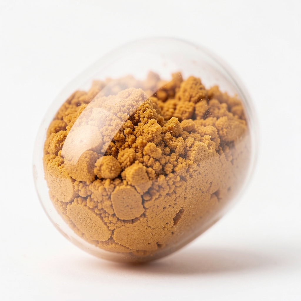 Close-up of supplement capsule granulation texture under bright controlled studio lighting, showing matte amber powder fill inside a clear food-grade capsule shell